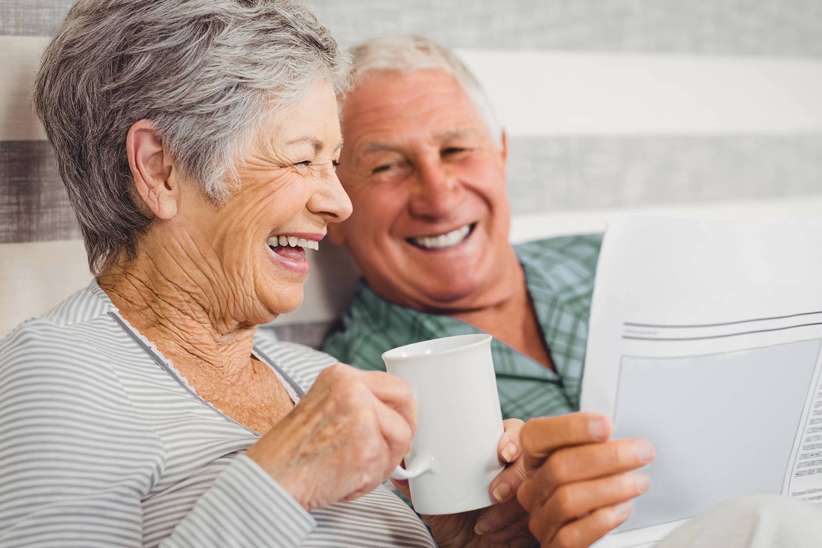 Elderly couple smiling and laughing while holding tea and medical paperwork, reflecting well-being with medical cannabis UK therapy